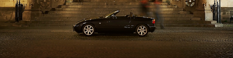 Coche negro aparcado de noche en el exterior de una casa grande, junto a unos escalones de piedra