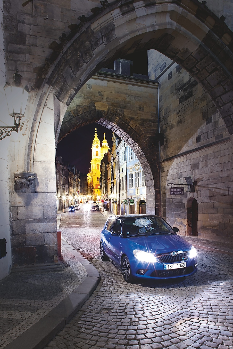 Coche azul aparcado bajo un arco en una calle empedrada de Praga de noche