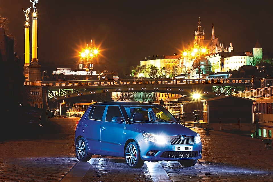 Coche azul aparcado en una calle de Praga con un puente y el castillo al fondo, de noche