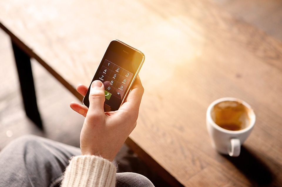 Hombre sosteniendo un teléfono móvil y bebiendo café